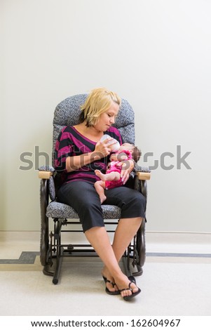 Full length of mid adult loving mother feeding milk to newborn baby girl while sitting on chair in hospital