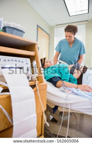 Nurse examining pregnant woman with report coming out from cardiotocograph machine in hospital