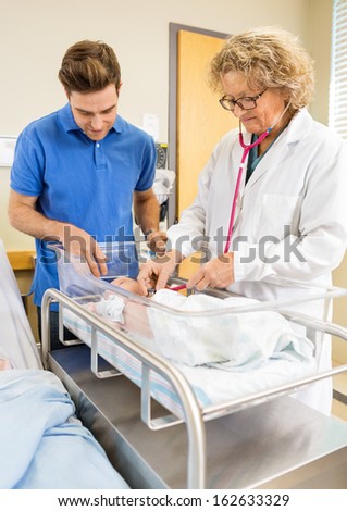 Female mature doctor examining newborn babygirl while father looking at her in hospital
