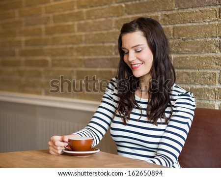 Attractive young woman looking at coffee cup while sitting in rustic cafe