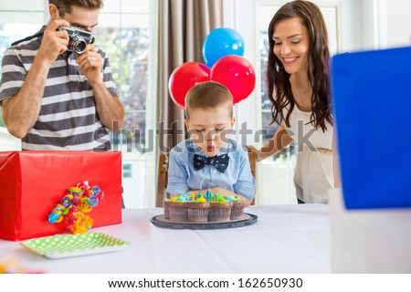 Father taking picture of son blowing out candles on cake at home