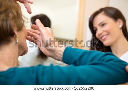 Senior woman inserting contact lens in optician store