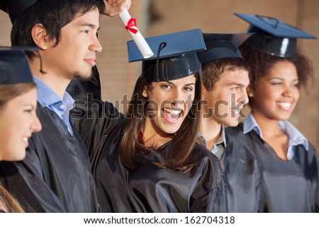 Portrait of excited female student holding certificate while standing with friends at college
