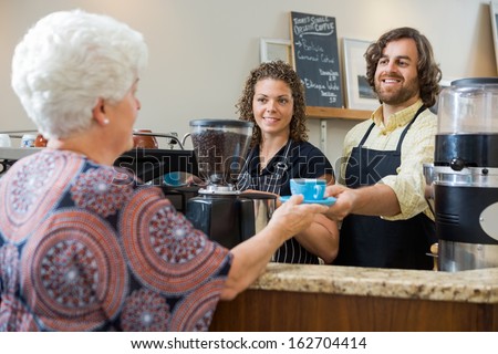 Mid adult waitress with colleague serving coffee to senior woman at counter in cafe