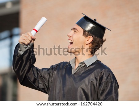 Excited male student holding diploma on graduation day in college