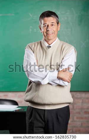 Portrait of confident male professor standing arms crossed in classroom