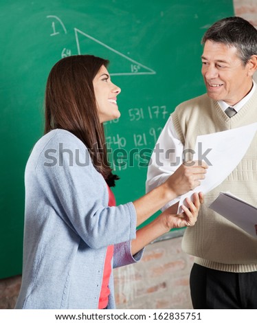Happy female student with exam result looking at teacher in classroom