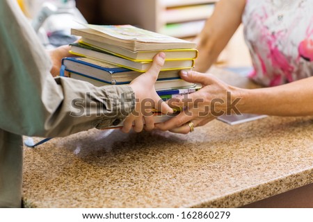 Cropped Image Of Female Librarian Taking Books From Boy At Checkout Counter In Library