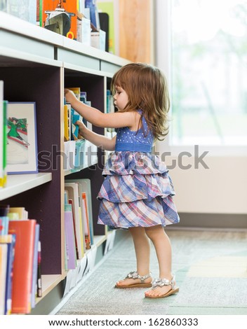 Full Length Side View Of Cute Girl Choosing Book From School Library