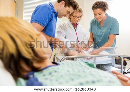 Female mature doctor examining newborn baby while standing by nurse and man with mother in foreground