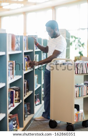 Full length of male librarian arranging books in shelf at library