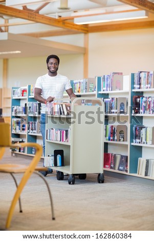Portrait of African American librarian with trolley of books smiling in bookstore