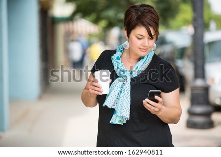 Young Woman Holding Disposable Coffee Cup While Text Messaging Through Smartphone Outdoors