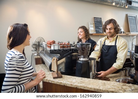 Female customer looking at baristas making coffee in cafeteria