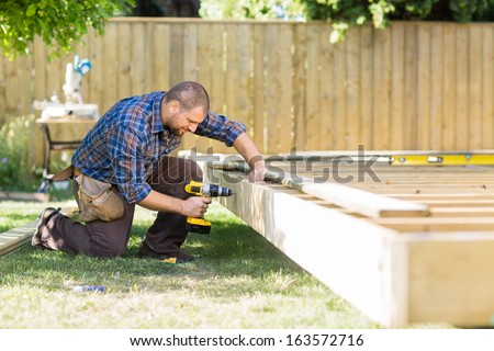 Full length of mid adult carpenter drilling wood at construction site