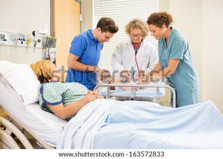 Female mature doctor examining newborn baby while parents and nurse looking at her in hospital