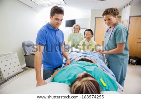 Smiling medical team and husband looking at pregnant woman during delivery in operating room