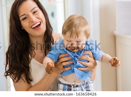 Mid adult mother holding baby boy with cake icing on face and hands at birthday party