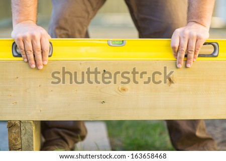 Cropped image of carpenter\'s hands using spirit level on wood at construction site