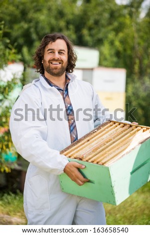 Portrait of happy male beekeeper carrying honeycomb crate at apiary