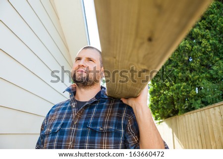 Mid adult carpenter carrying wooden plank on shoulder at construction site