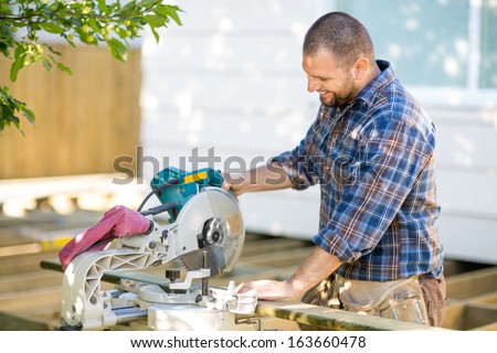 Happy mid adult carpenter cutting wood using table saw at construction site