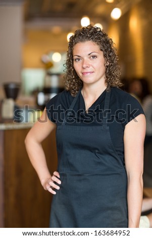 Portrait of beautiful mid adult waitress standing with hand on hip in cafe