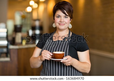 Portrait Of Confident Waitress Holding Coffee Cup While Standing In Cafe