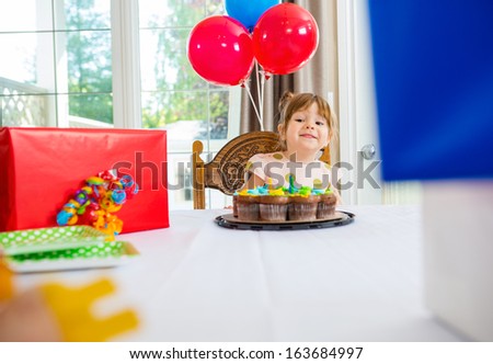 Birthday girl looking at presents with cake on table at home
