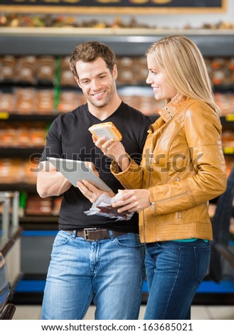 Smiling couple using digital tablet while purchasing meat at butcher\'s shop