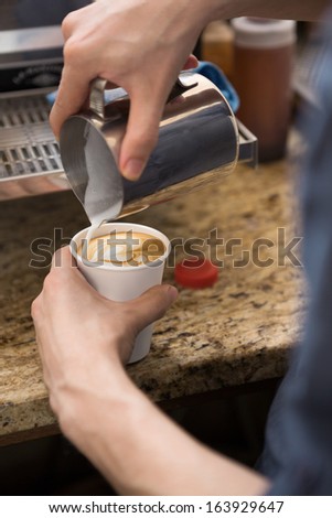 Cropped image of barista making design on cappuccino in coffeeshop