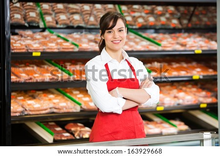 Portrait of beautiful saleswoman standing arms crossed at counter in butcher\'s shop