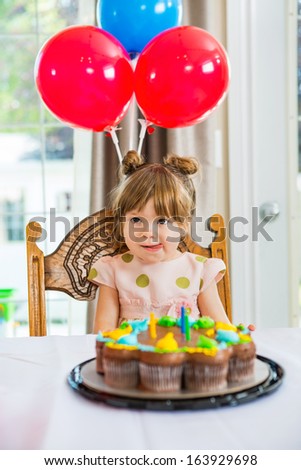 Girl licking lips while sitting in front of birthday cake at home