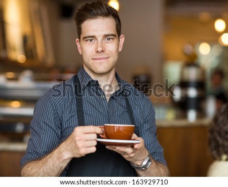 Portrait of male barista standing in cafe with cup of coffee
