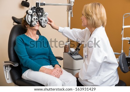 Female optician using phoropter to examine senior woman\'s eyes