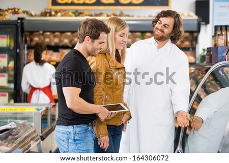 Happy worker assisting couple in buying meat at butcher\'s shop
