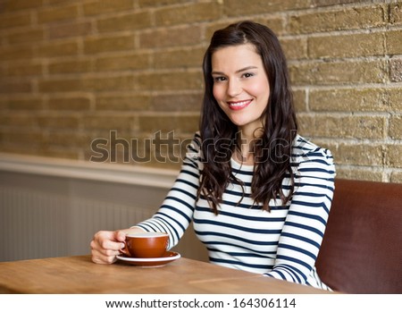 Portrait of attractive young woman sitting with coffee cup at table in cafe