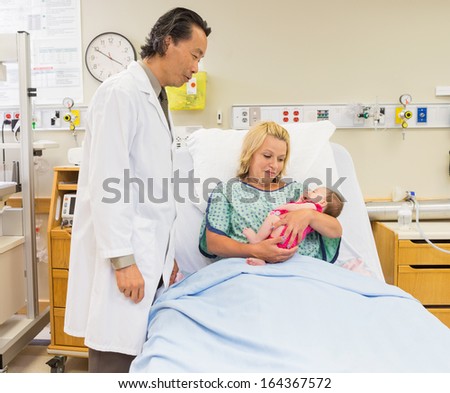 Loving Mother And Doctor Looking At Newborn Baby Girl In Hospital Room