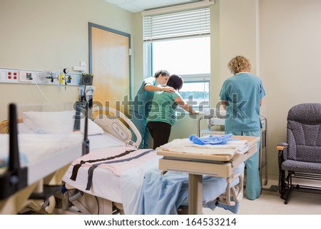 Friendly female nurse comforting pregnant woman standing at window in hospital room
