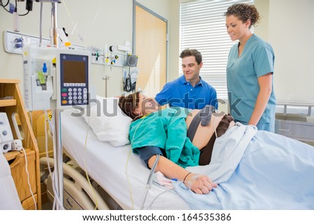 Happy nurse and man looking at pregnant woman lying on bed in hospital