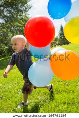 Full length of happy boy with colorful balloons walking in park