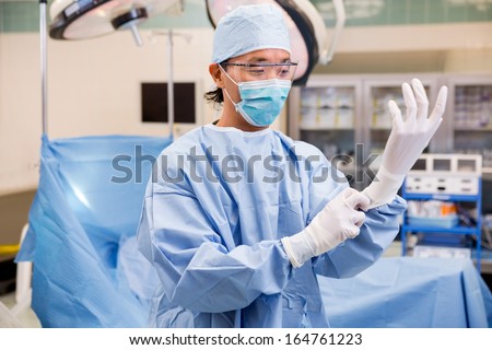 Mid adult male surgeon wearing surgical gloves in operation room