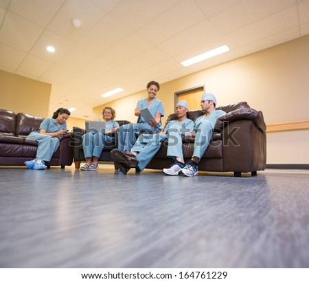 Full length of multiethnic medical team using technologies in hospital\'s waiting room