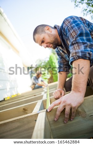 Mid adult carpenter measuring wood with tape while coworker assisting him at site