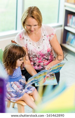Mature teacher with schoolgirl reading book in library