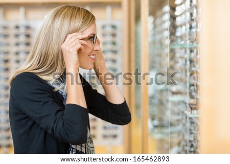 Side view of mid adult woman trying on eyeglasses in optician store