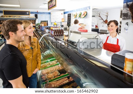 Smiling young saleswoman attending customers at butcher\'s shop