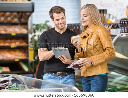 Couple using digital tablet while checking ingredients of product at butcher\'s shop