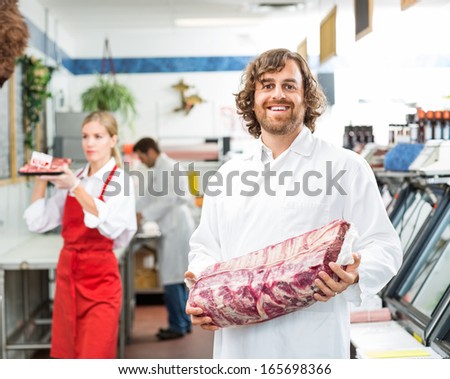Portrait Of Happy Butcher Holding Meat Package While Standing In Store