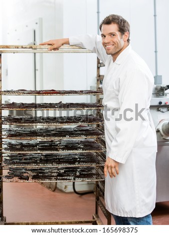 Portrait of happy male worker standing by rack of beef jerky at butcher\'s shop